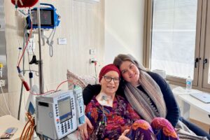 Abbey sitting with her mum in hospital as her mum receives Abbey's donated stem cells