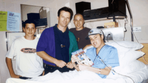 Allan in hospital with his brothers and Australian cricketer Steve Waugh standing beside him