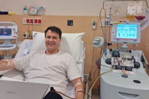 Man connected to apheresis machine donating stem cells smiling at camera